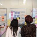 three women standing in front of a whiteboard covered in writing and colourful post-it notes
