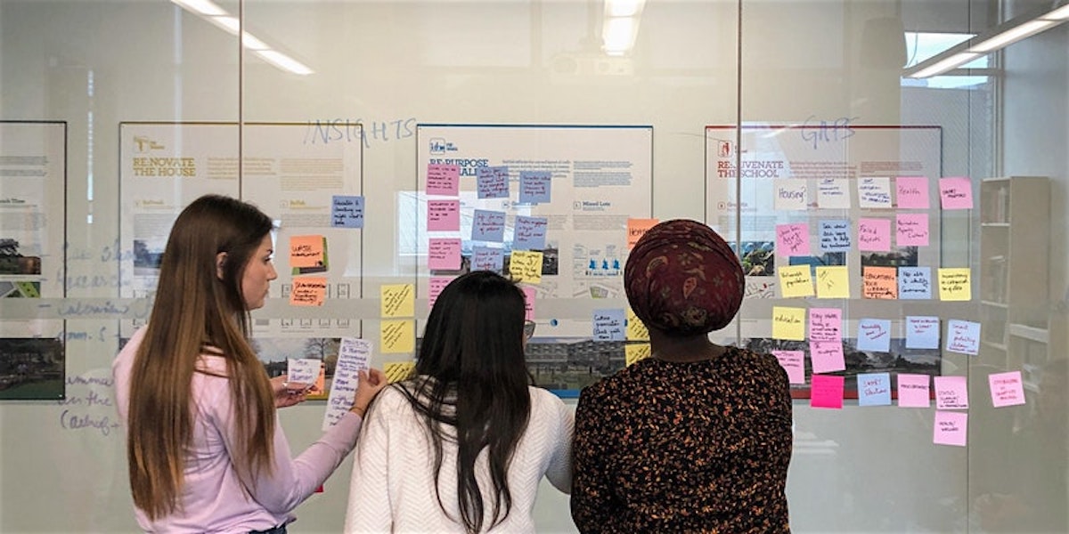 three women standing in front of a whiteboard covered in writing and colourful post-it notes
