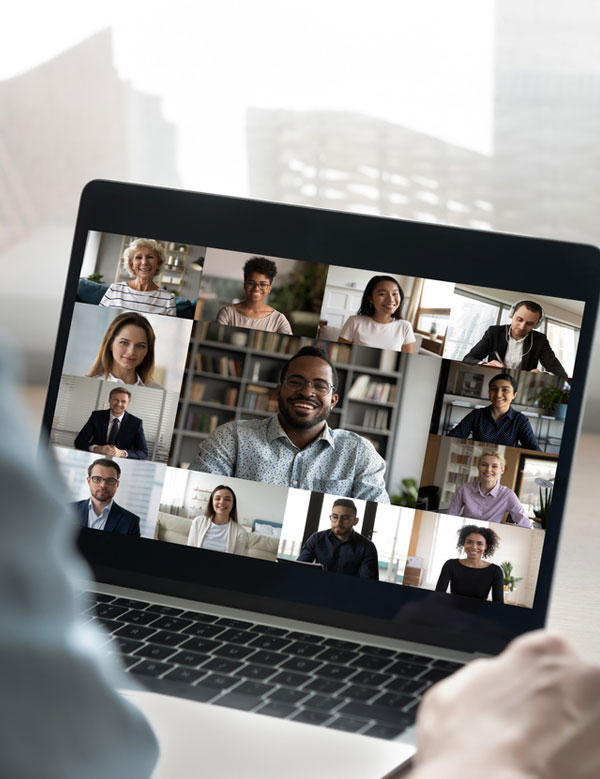 A person outside of the frame looks at a laptop, where a video call of a dozen people is taking place
