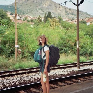 person in summer clothes standing in front of train tracks smiling at camera