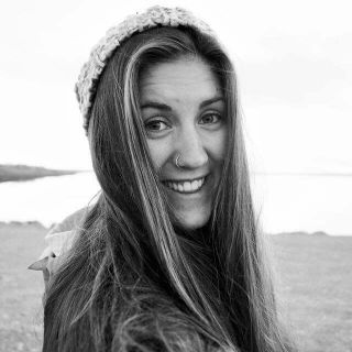 person with long hair and a nose ring at a beach smiling at camera