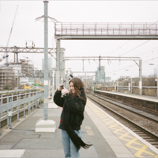 person standing on a train platform taking a picture with a phone and smiling