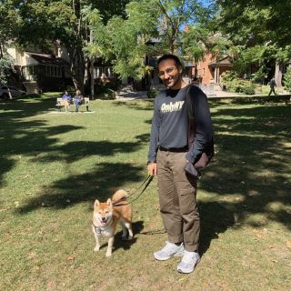 person standing in a park during the summer with a dog on a leash smiling