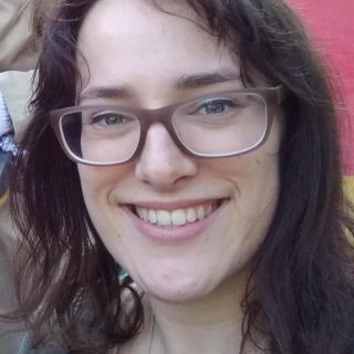 person with long brown hair wearing glasses smiling at camera