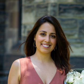 person with long dark hair wearing a pink top smiling directly at camera