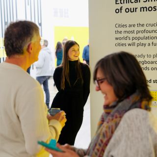 person with long hair leaning against a banner smiling widely
