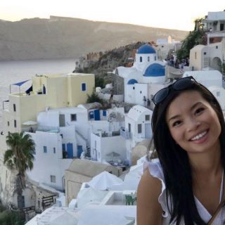 person with long hair wearing a white top smiling with the ocean behind them