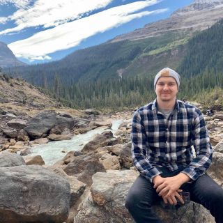 person sitting on a rock wearing hiking gear in front of mountains
