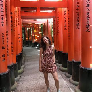 person wearing a summer dress and white sneakers standing in red archway