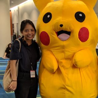 person wearing a dark tshirt and jeans with a lanyard standing next to a giant pikachu