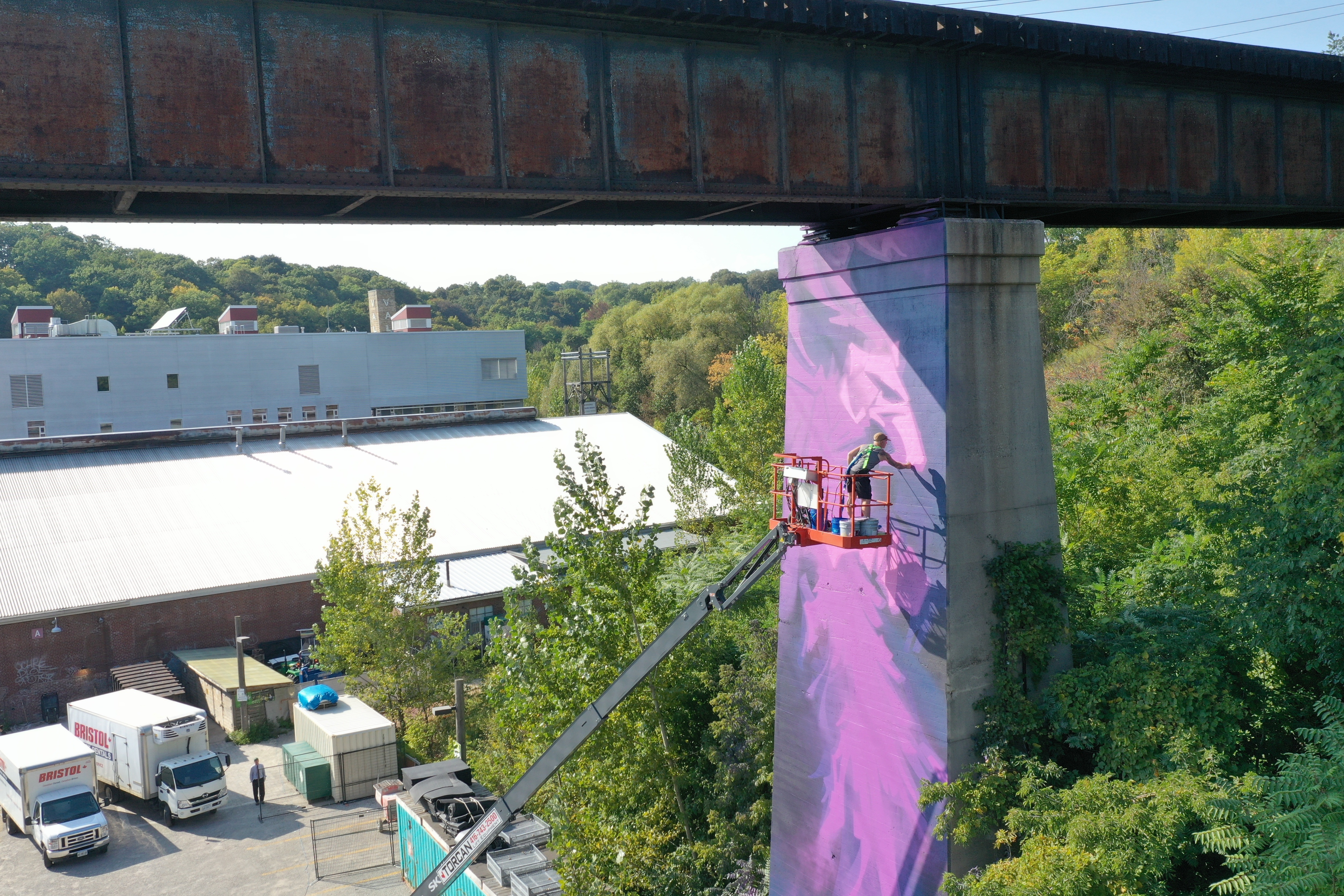 An artist painting a mural onto the side of a railway pillar
